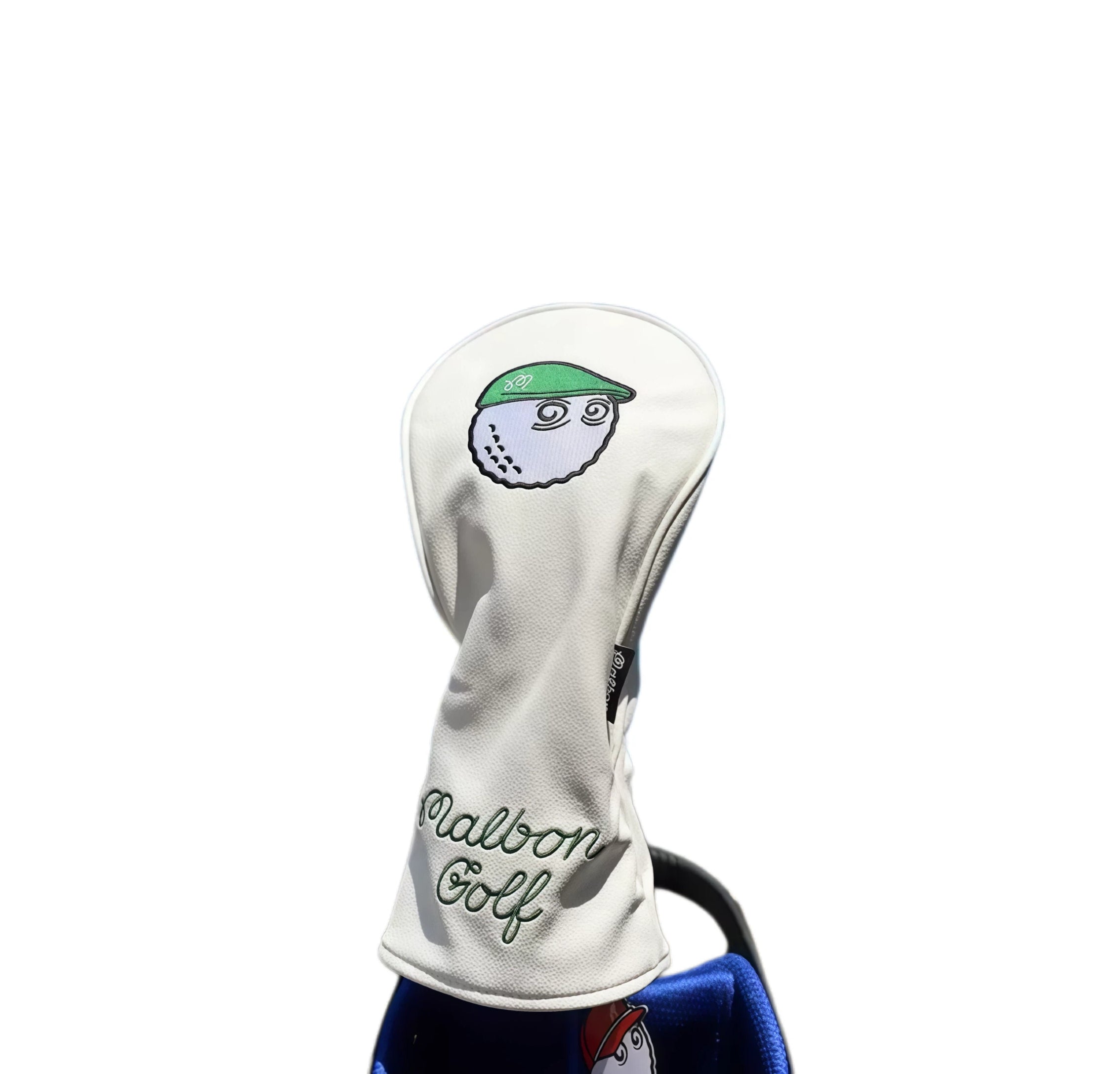 Close-up of a white Malbon Golf driver headcover featuring a cartoon golf ball character wearing a green baseball cap and embroidered "Malbon Golf" text — premium protection with a fun, personalized touch for your driver.