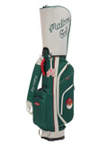 Full side profile of Malbon Golf Heritage stand bag in green, showcasing adjustable shoulder strap, cartoon golf ball mascot, and embroidered “Malbon Golf” branding